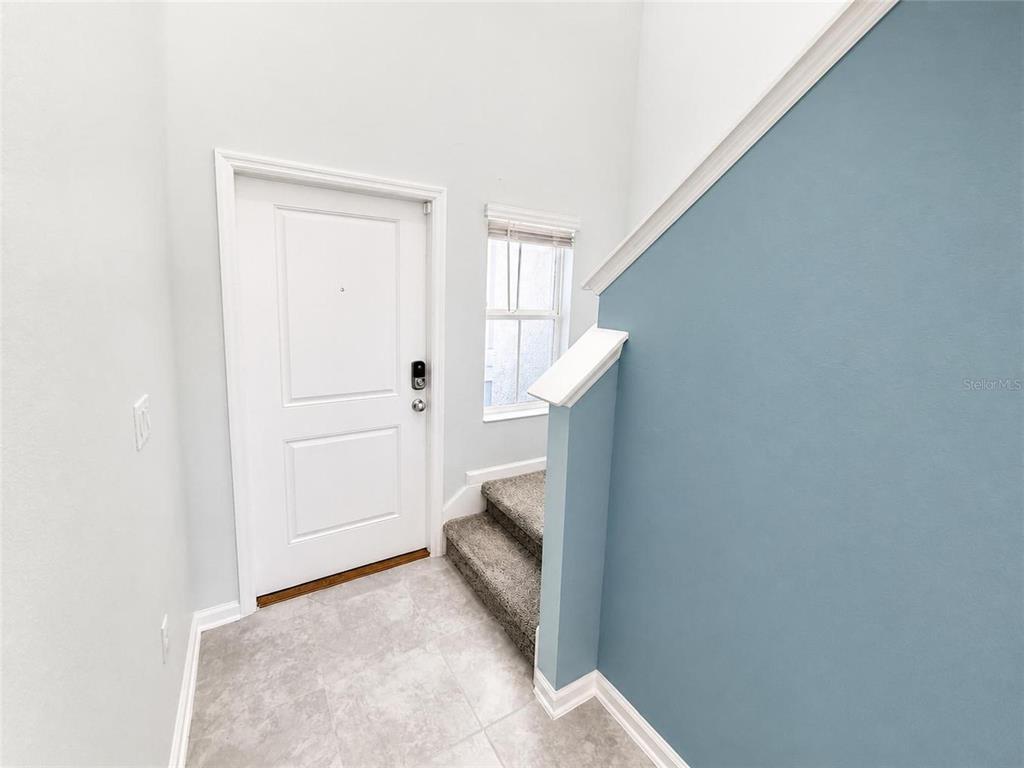 An entryway features a white front door, gray tiled flooring, and carpeted stairs — 5632 LOGGIA LANE, KISSIMMEE, FL