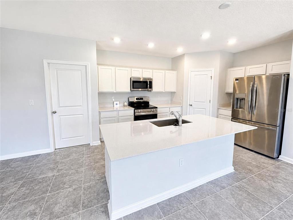 A kitchen features white cabinets, stainless steel appliances, a center island, and gray tile flooring — 5632 LOGGIA LANE, KISSIMMEE, FL