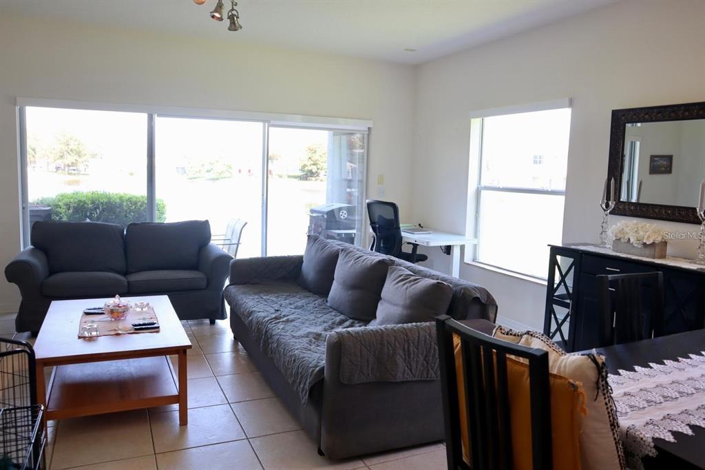 A living room features two gray sofas, a coffee table, and a desk near windows — 9395 FLOWERING COTTONWOOD ROAD UNIT 32, ORLANDO, FL