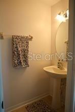 A small bathroom features a pedestal sink, an oval mirror, and a patterned hand towel — 9395 FLOWERING COTTONWOOD ROAD UNIT 32, ORLANDO, FL