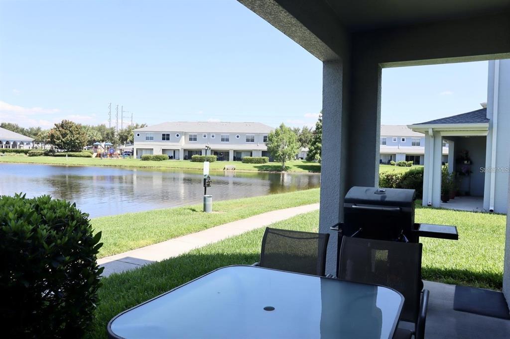 A covered patio overlooks a pond with a glass table and a grill — 9395 FLOWERING COTTONWOOD ROAD UNIT 32, ORLANDO, FL