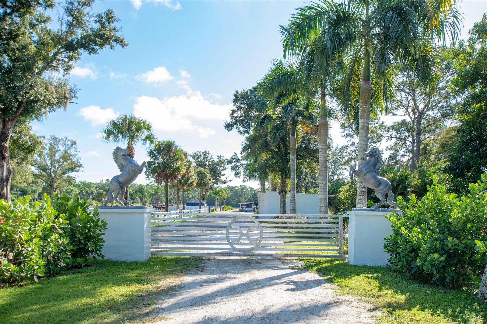 A gated entrance with two horse statues on white pillars leads to a dirt driveway — 1044 D Road, FL 33470, FL