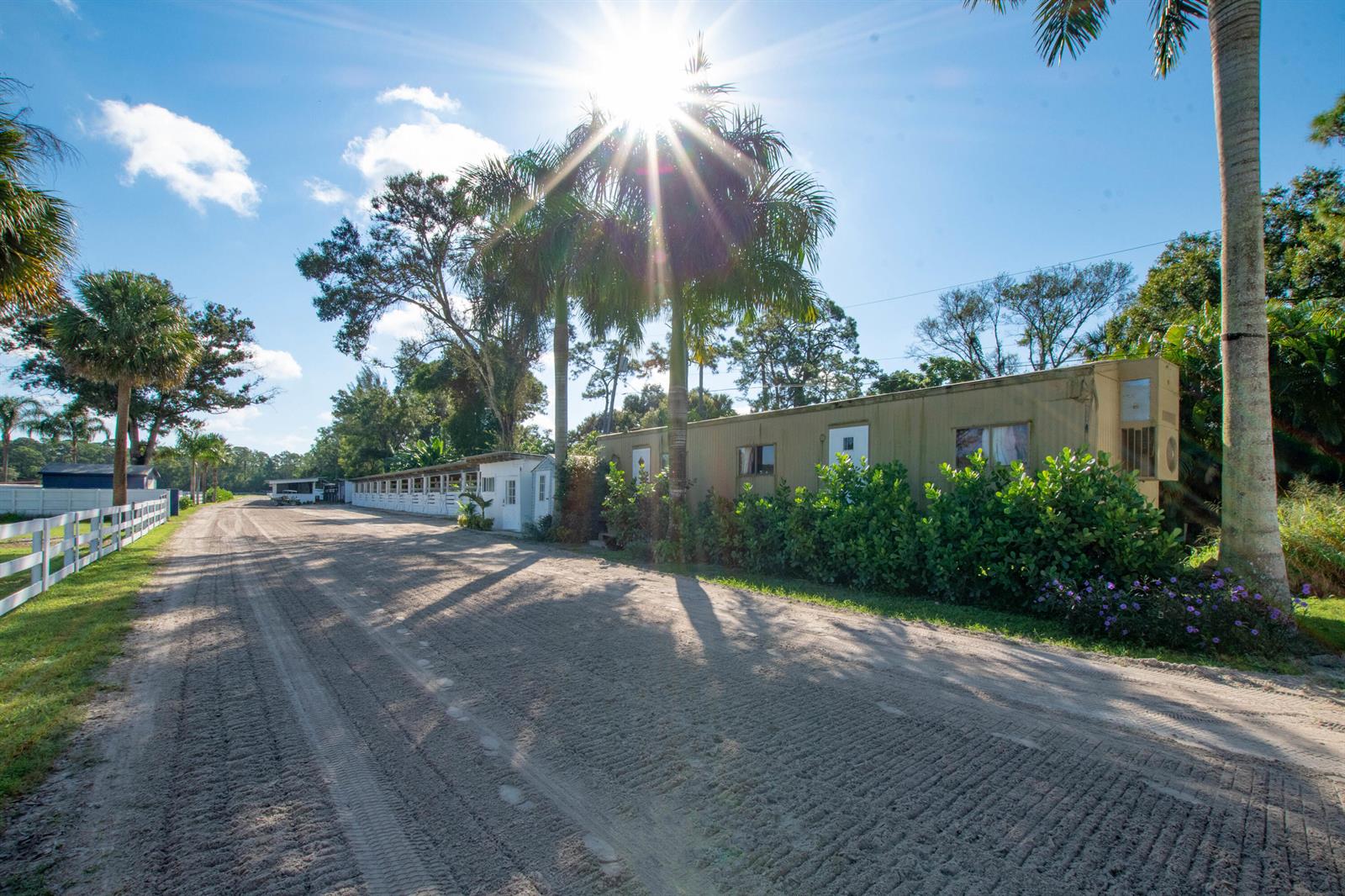A dirt driveway leads past a long, tan mobile home and a row of horse stalls — 1044 D Road, FL 33470, FL