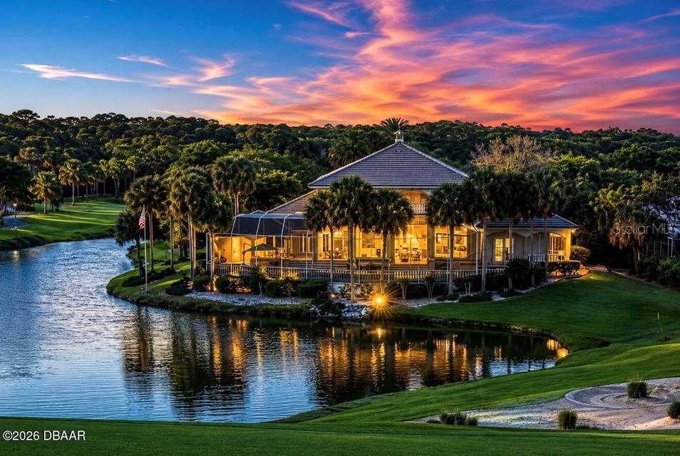 A large house with a screened-in porch sits beside a lake at sunset — 25 SAN MARCO COURT, PALM COAST, FL
