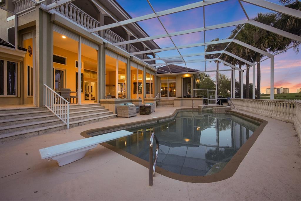 A swimming pool with a diving board sits inside a screened enclosure behind a house — 25 SAN MARCO COURT, PALM COAST, FL