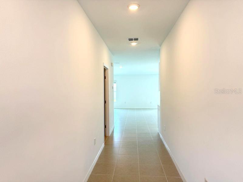 A hallway with light-colored walls and tile flooring leads toward an open living area — 38396 PINDOS DRIVE, DADE CITY, FL