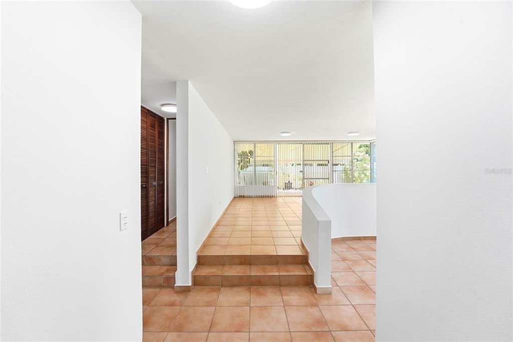 A tiled hallway leads to a sunken living area with large windows and white walls — 115 PASEO REAL, DORADO, PR