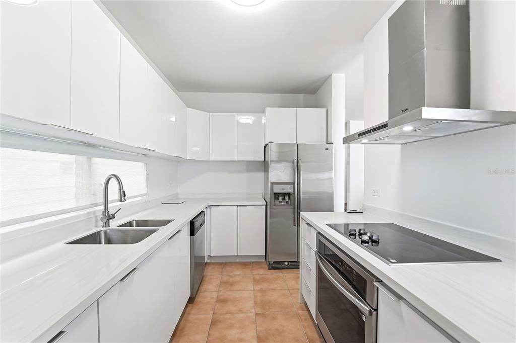 A modern kitchen features white cabinets, stainless steel appliances, and light-colored countertops over tile flooring — 115 PASEO REAL, DORADO, PR