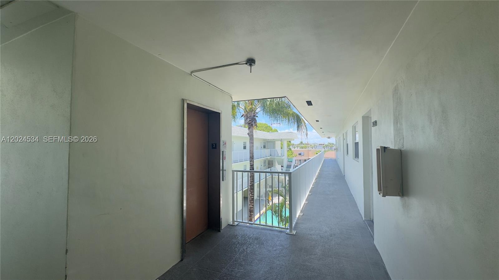 An outdoor apartment hallway features a metal railing overlooking a courtyard with a pool — 12890 NE 8th Ave # 302, North Miami FL 33161, NORTH MIAMI, FL