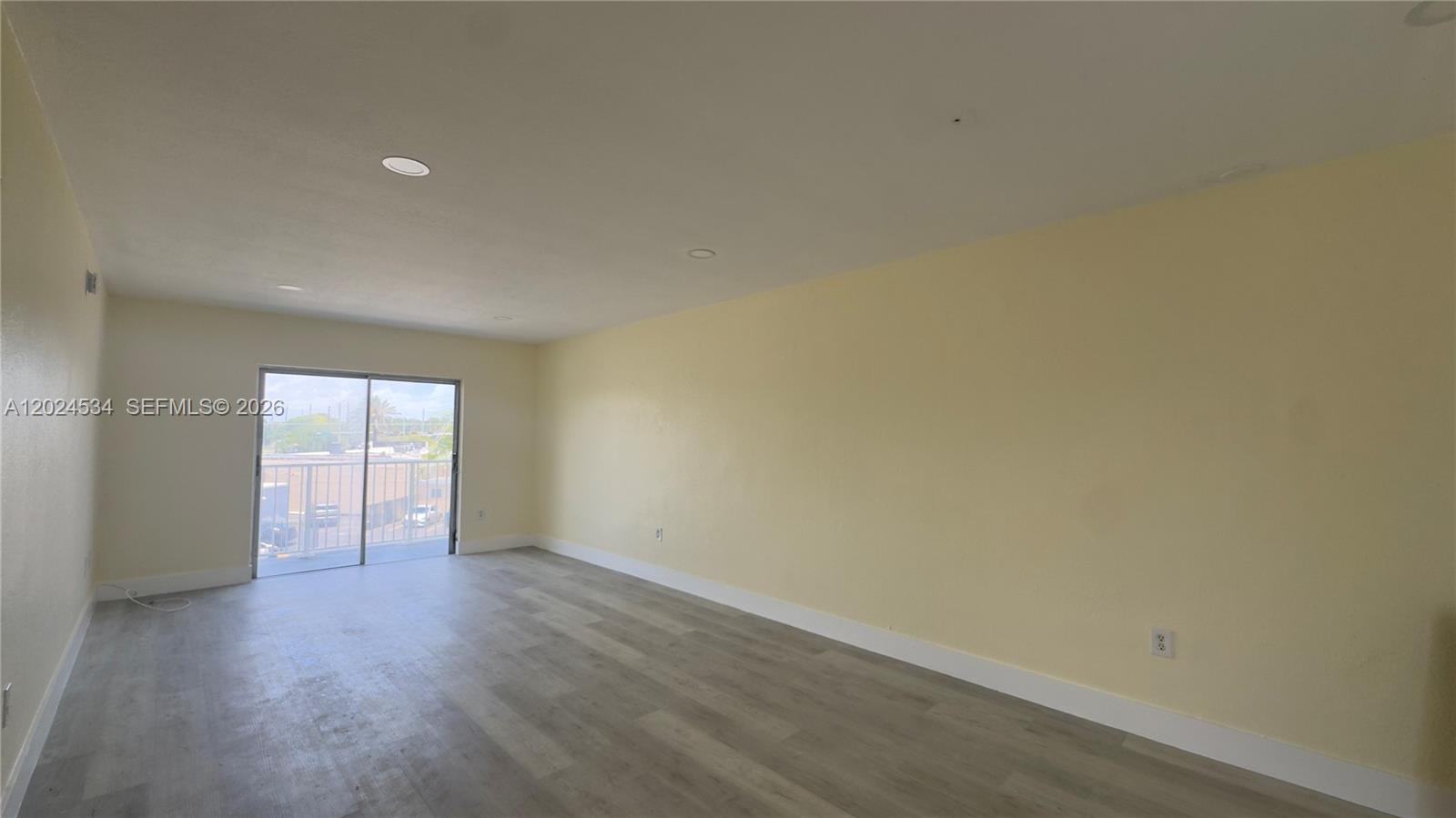 An empty room features light yellow walls, wood-look flooring, recessed lighting, and a sliding glass door — 12890 NE 8th Ave # 302, North Miami FL 33161, NORTH MIAMI, FL