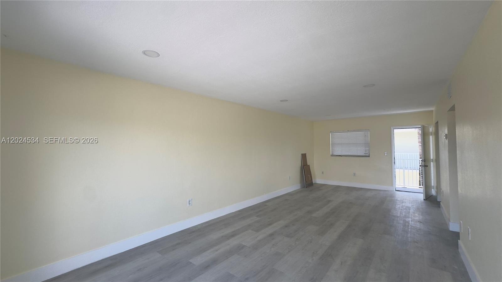 An empty room features light yellow walls, gray wood-look flooring, recessed lighting, and a door — 12890 NE 8th Ave # 302, North Miami FL 33161, NORTH MIAMI, FL