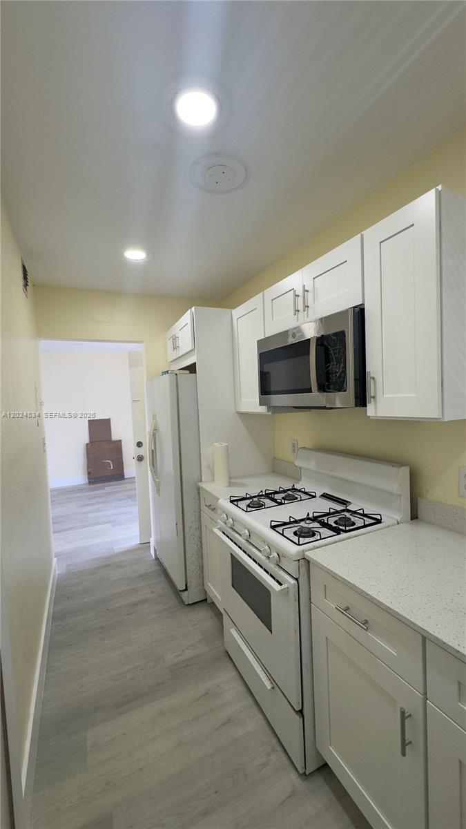 A galley kitchen features white cabinets, a gas range, and light-colored flooring — 12890 NE 8th Ave # 302, North Miami FL 33161, NORTH MIAMI, FL