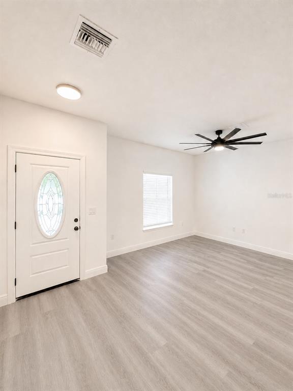 A bright room features light wood-look flooring, a white front door, and a ceiling fan — 545 N LINCOLN STREET, DAYTONA BEACH, FL