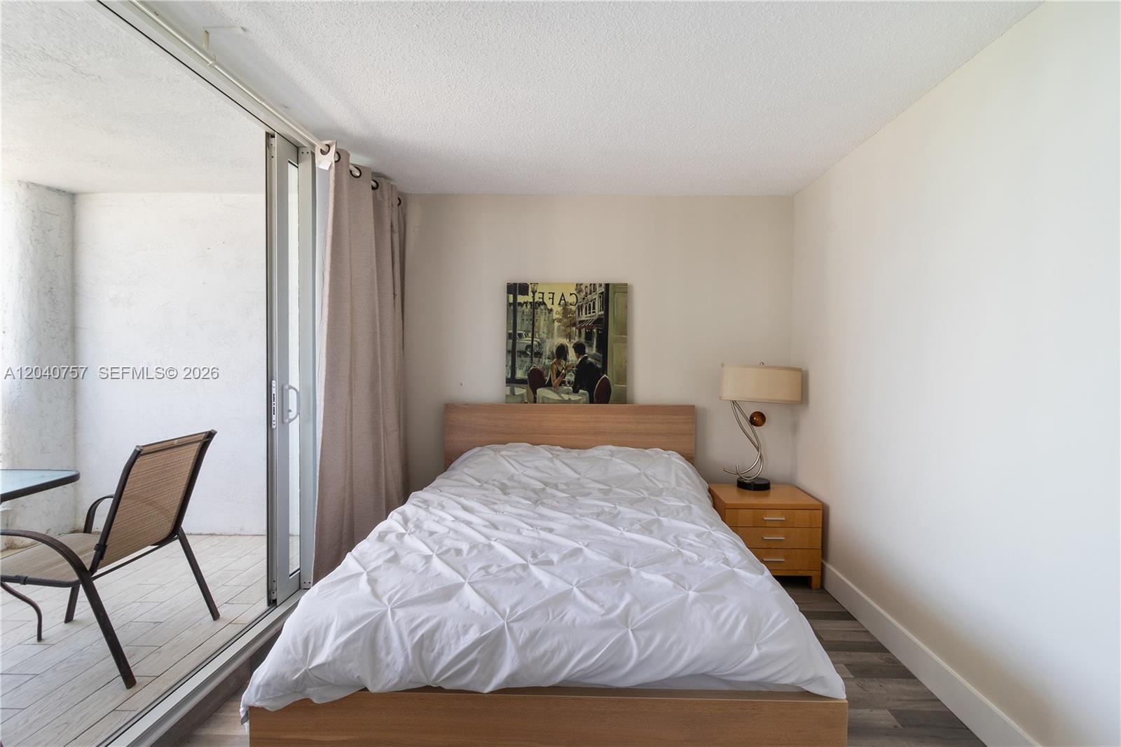 A bedroom features a bed with a white comforter, a nightstand, and a sliding glass door — 1717 N Bayshore Dr # 2837, Miami FL 33132, MIAMI, FL