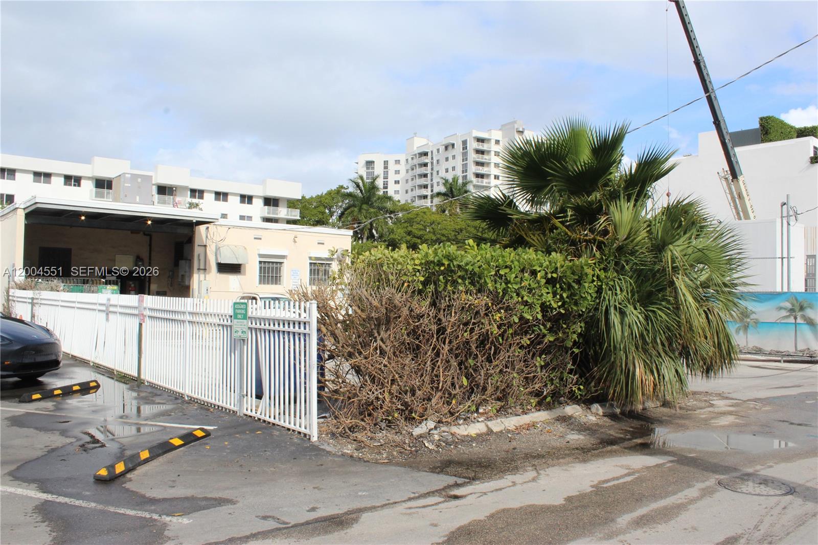 A white fence encloses a parking area next to a building and palm trees — 1661 West Ave, Miami Beach FL 33139, MIAMI BEACH, FL