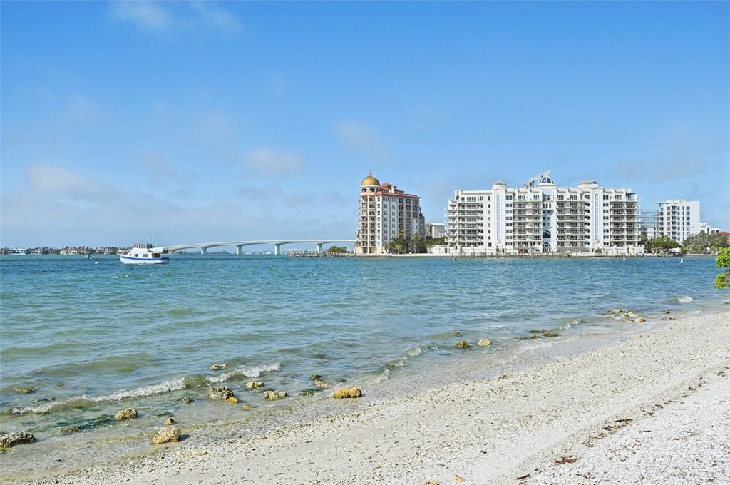 A view of a sandy beach with a boat, a bridge, and waterfront apartment buildings — 1771 RINGLING BOULEVARD UNIT 1001, SARASOTA, FL