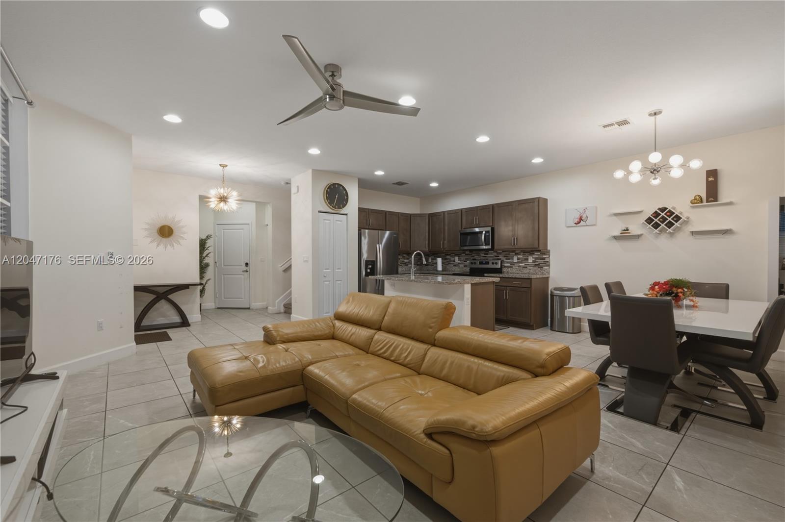 An open-concept living and dining area features a tan leather sectional, kitchen, and tile flooring — 4812 NW 48th Ter, Tamarac FL 33319, TAMARAC, FL