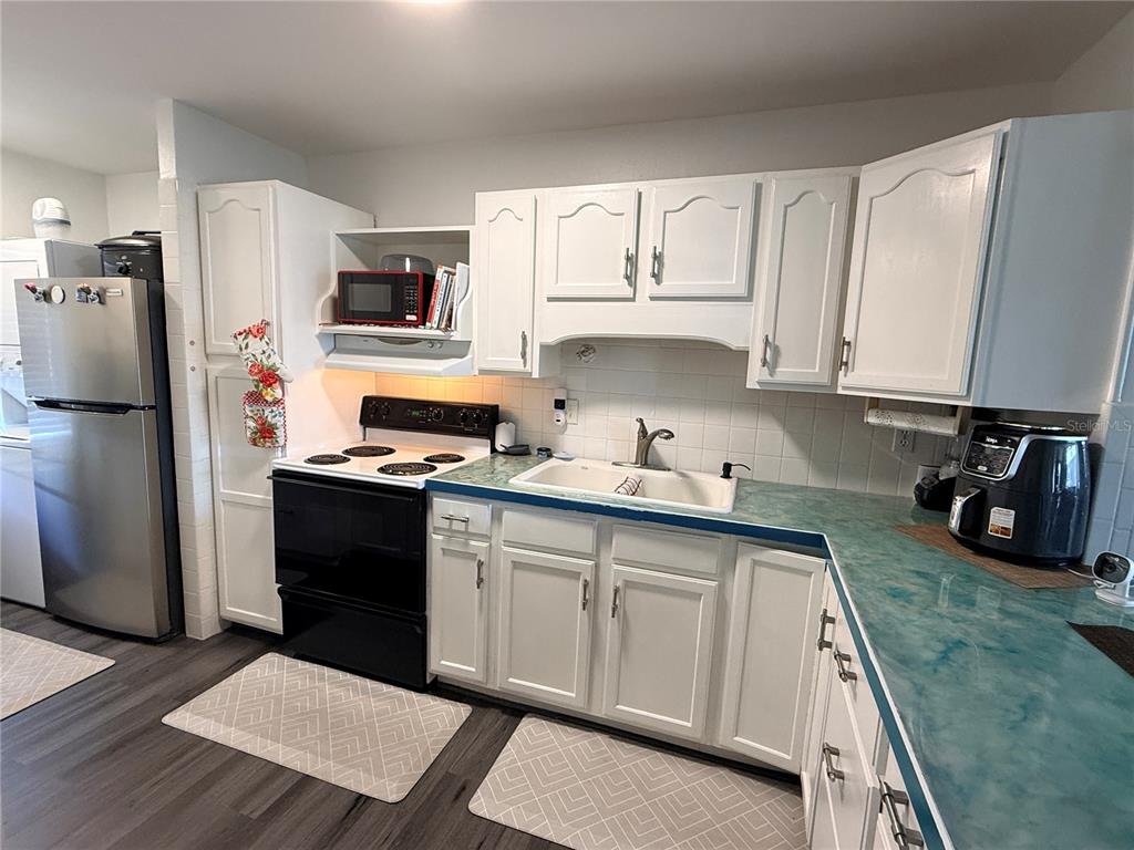 A kitchen features white cabinets, a teal countertop, a black stove, and a stainless refrigerator — 1437 N ATLANTIC AVENUE UNIT 410, DAYTONA BEACH, FL