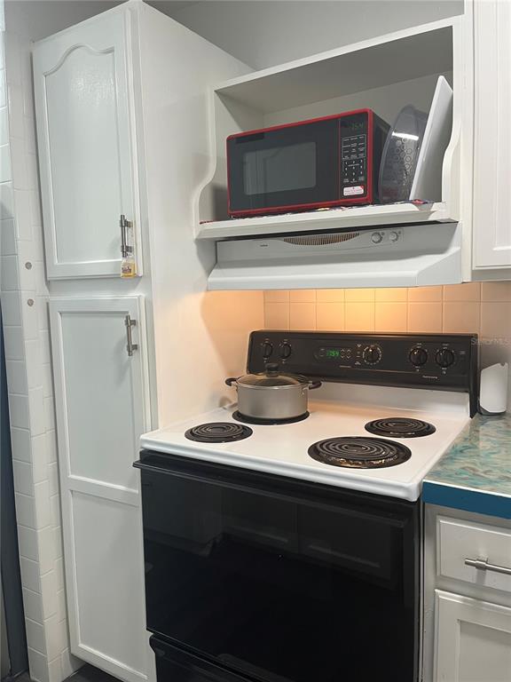 A kitchen features a black electric stove, a red microwave, and white cabinetry — 1437 N ATLANTIC AVENUE UNIT 410, DAYTONA BEACH, FL