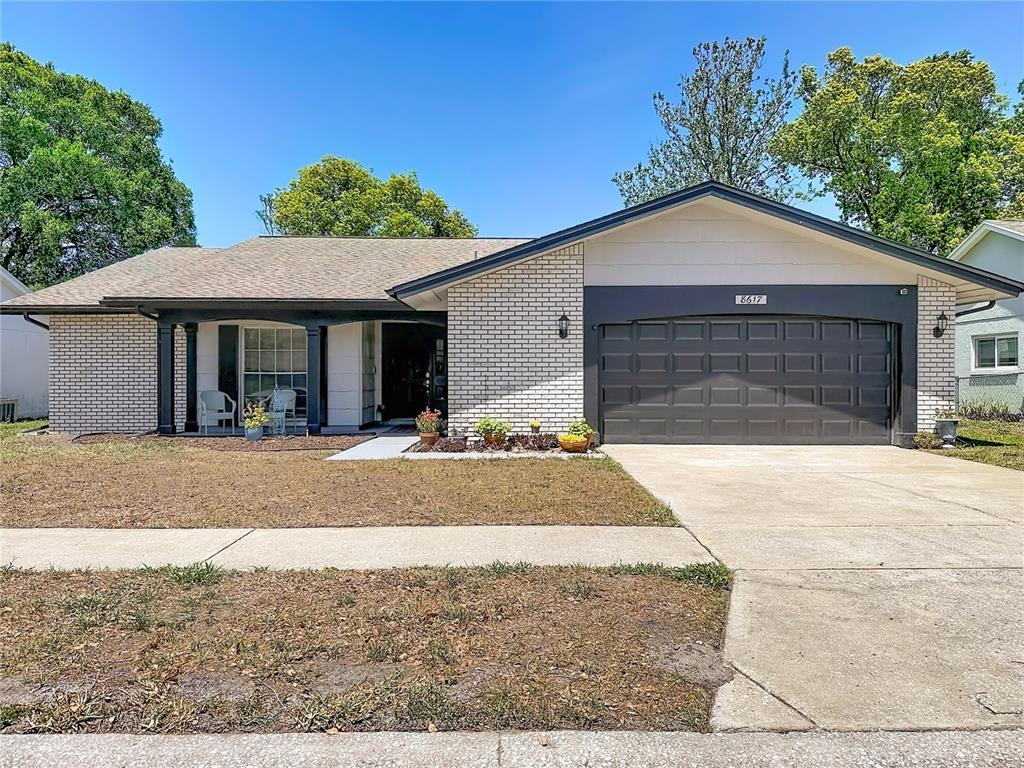 A single-story house features a white brick exterior, a dark garage door, and a front porch — 8617 STONEHEDGE WAY, HUDSON, FL