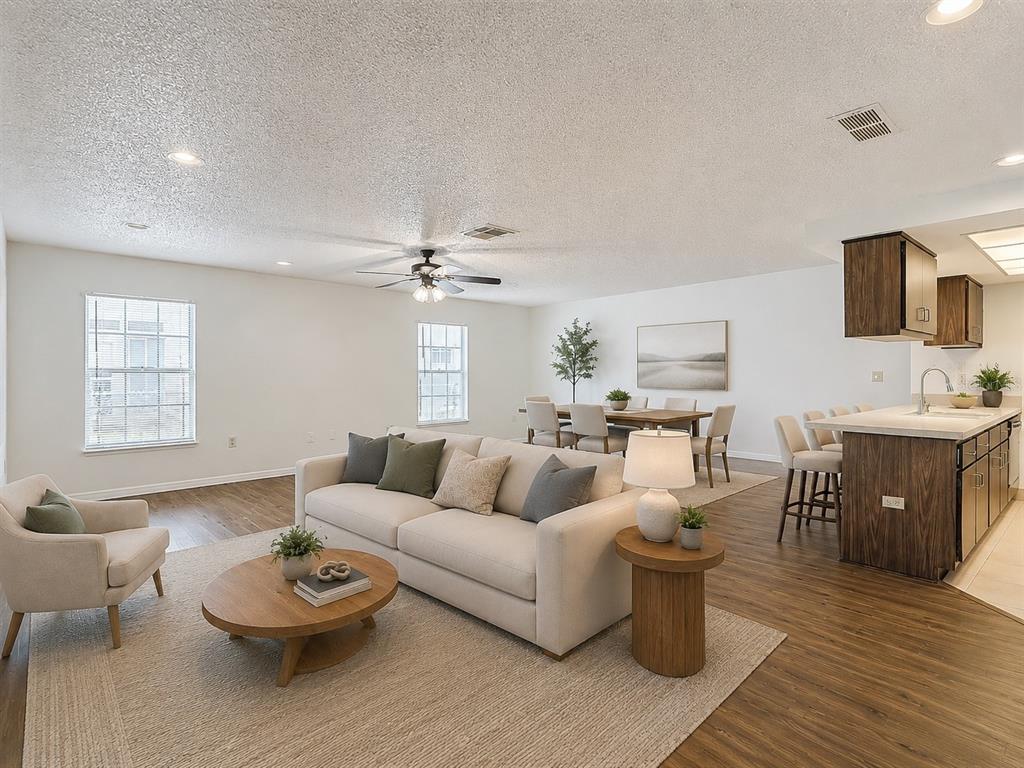 An open-concept living and dining area features wood-look flooring, a kitchen island, and neutral furniture — 8617 STONEHEDGE WAY, HUDSON, FL