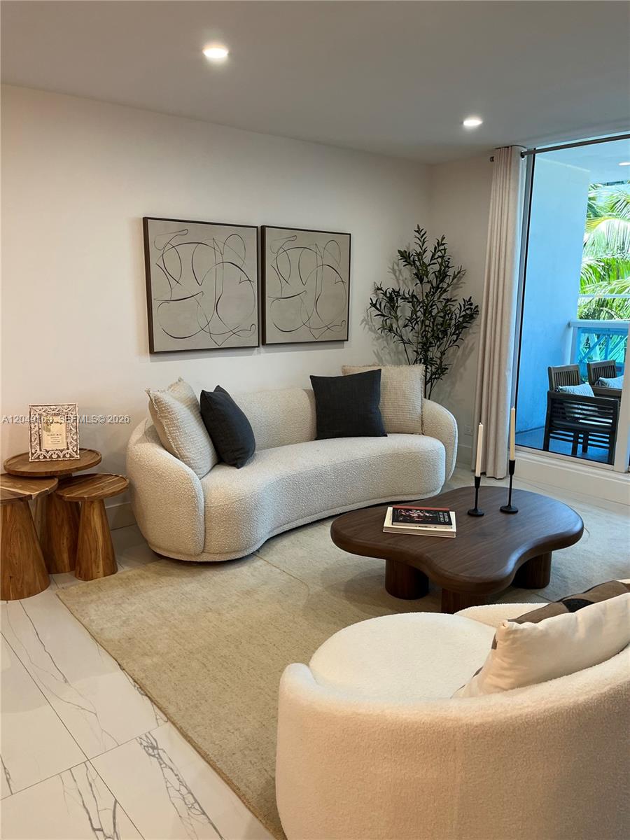 A living room features a curved cream sofa, a wooden coffee table, and abstract wall art — 2301 Collins Ave # 326, Miami Beach FL 33139, MIAMI BEACH, FL