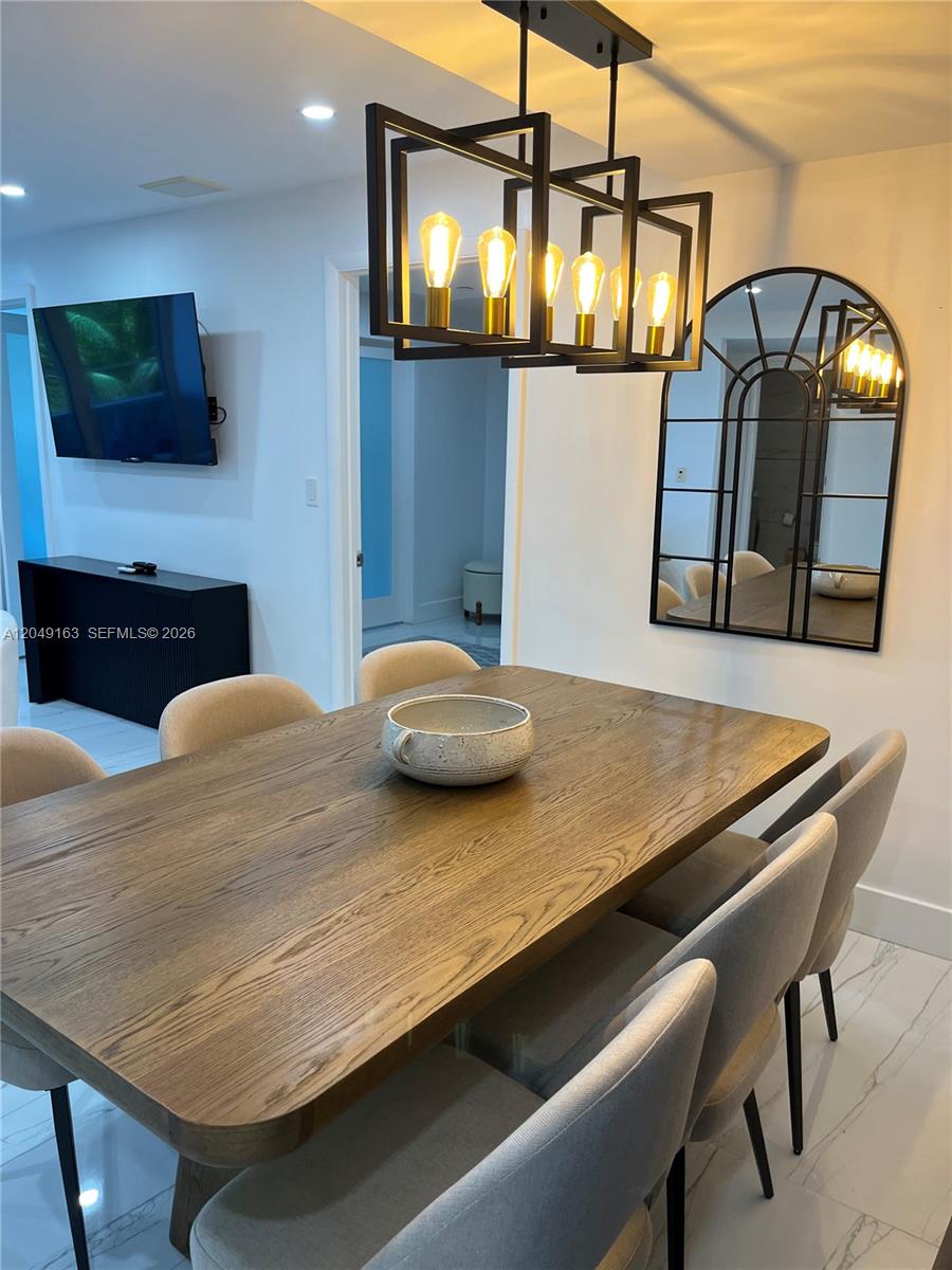 A dining room features a wooden table, upholstered chairs, a rectangular chandelier, and a wall mirror — 2301 Collins Ave # 326, Miami Beach FL 33139, MIAMI BEACH, FL
