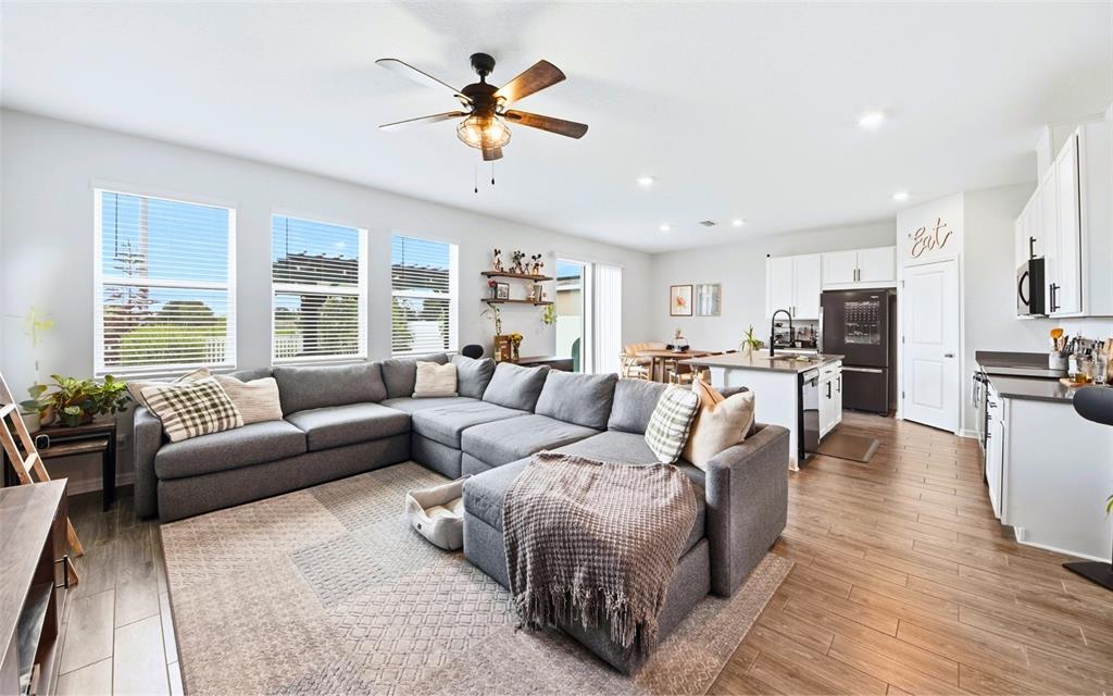 A spacious open-concept living room and kitchen feature gray sectional seating and wood-look flooring — 11873 BRIGHTON KNOLL LOOP, RIVERVIEW, FL