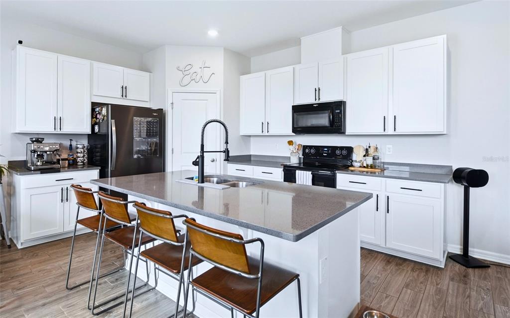 A kitchen features white cabinets, a gray island with bar stools, and stainless steel appliances — 11873 BRIGHTON KNOLL LOOP, RIVERVIEW, FL