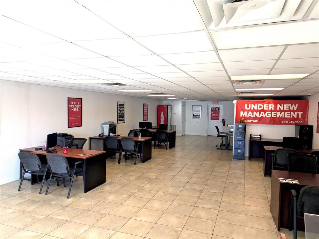 An office space features multiple desks, chairs, tiled flooring, and a large red management banner — 837 8TH AVENUE W UNIT 837, PALMETTO, FL