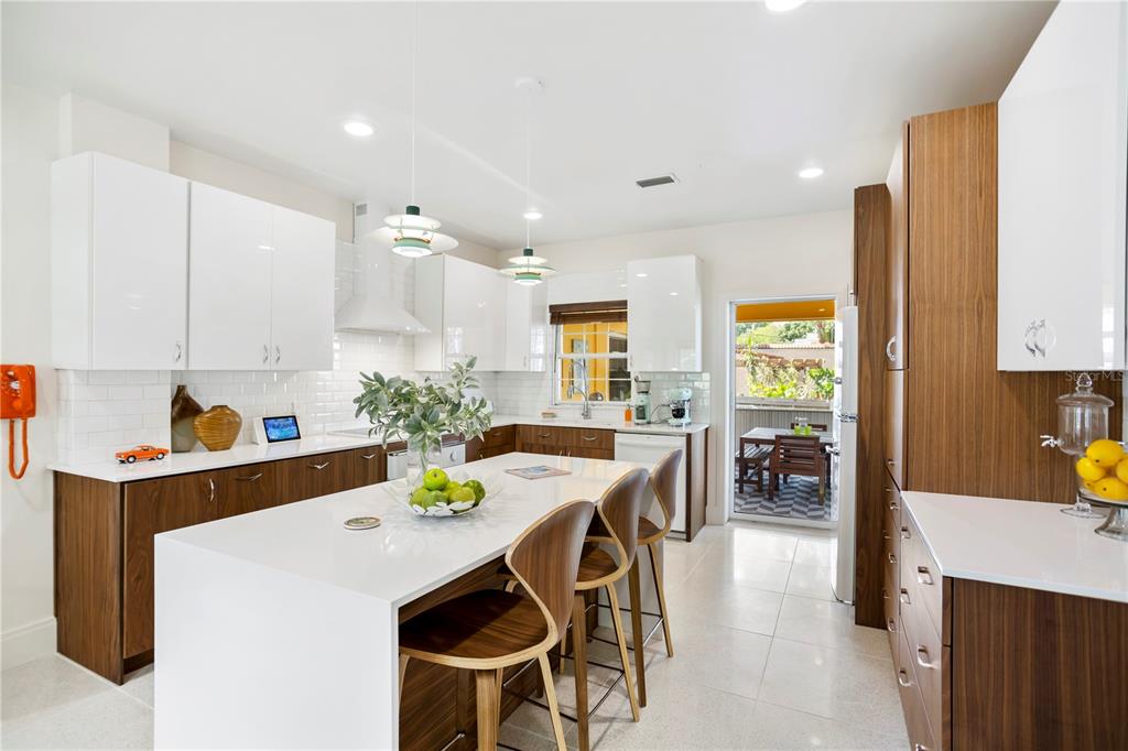 A modern kitchen features white upper cabinets, wood-toned lower cabinets, a central island, and bar seating — 2217 BREVARD ROAD NE, ST PETERSBURG, FL