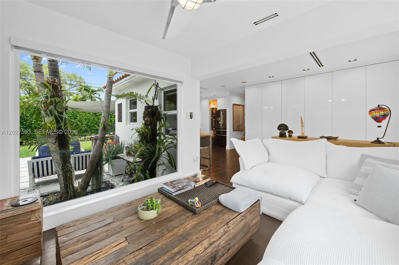 A living room with a large window overlooking a patio and a wooden coffee table — 39 Montilla Ave, Coral Gables FL 33134, CORAL GABLES, FL
