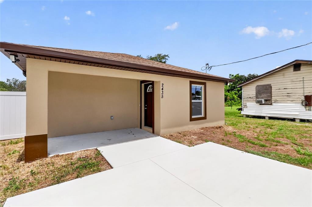 A tan house exterior features a covered front porch, brown trim, and a concrete walkway — 2435 5TH ST NE, WINTER HAVEN, FL