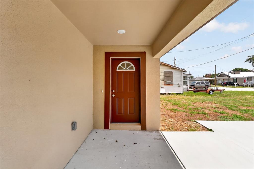 A covered concrete porch leads to a brown front door with a semi-circular window — 2435 5TH ST NE, WINTER HAVEN, FL