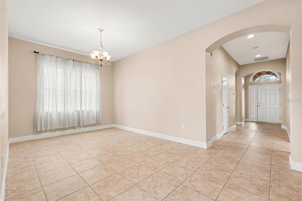 An empty dining room with beige walls, tile flooring, a chandelier, and a front entryway — 7614 ATWOOD DRIVE, WESLEY CHAPEL, FL