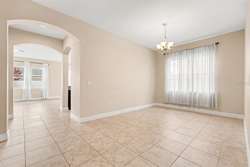 A dining room with beige walls, tile flooring, a chandelier, and an arched entryway — 7614 ATWOOD DRIVE, WESLEY CHAPEL, FL