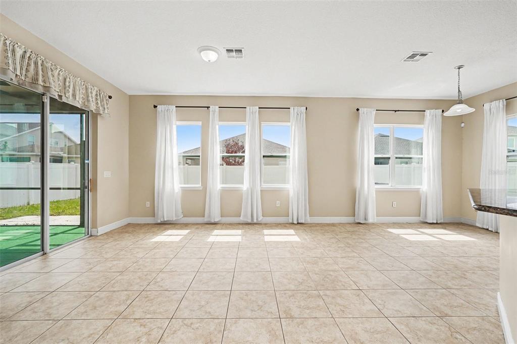 An open-concept room with tile flooring, large windows with white curtains, and a sliding door — 7614 ATWOOD DRIVE, WESLEY CHAPEL, FL