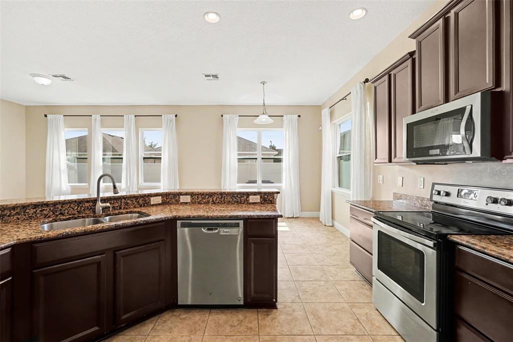 A kitchen with dark wood cabinets, granite countertops, stainless steel appliances, and tile flooring — 7614 ATWOOD DRIVE, WESLEY CHAPEL, FL
