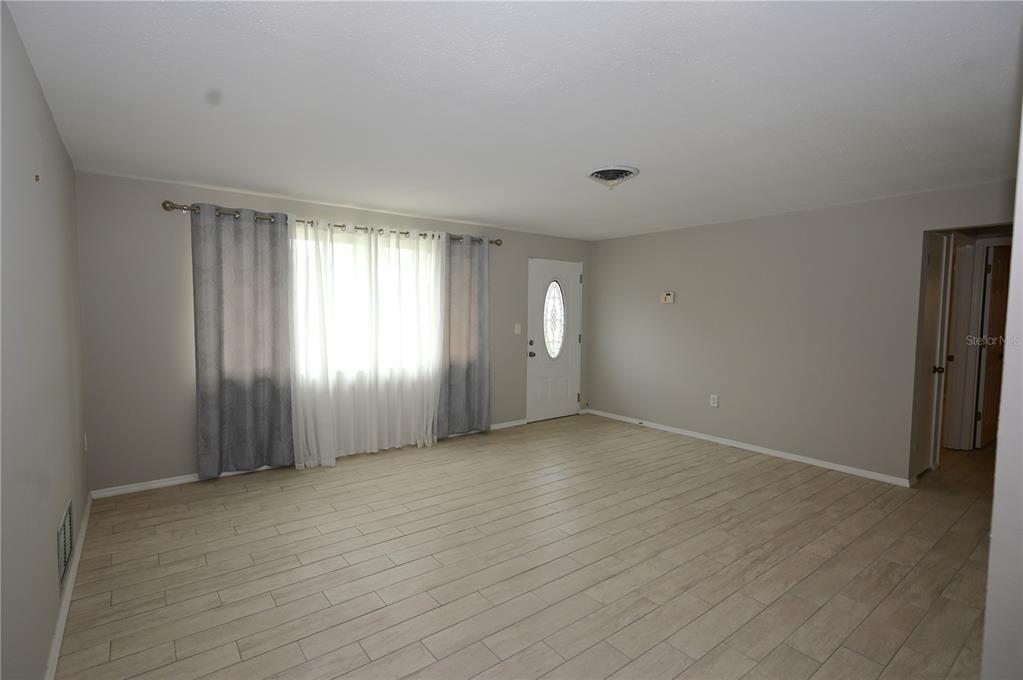 An empty living room features light-colored wood-look tile flooring, gray walls, and a front door — 1620 MORNING DOVE LANE, ENGLEWOOD, FL