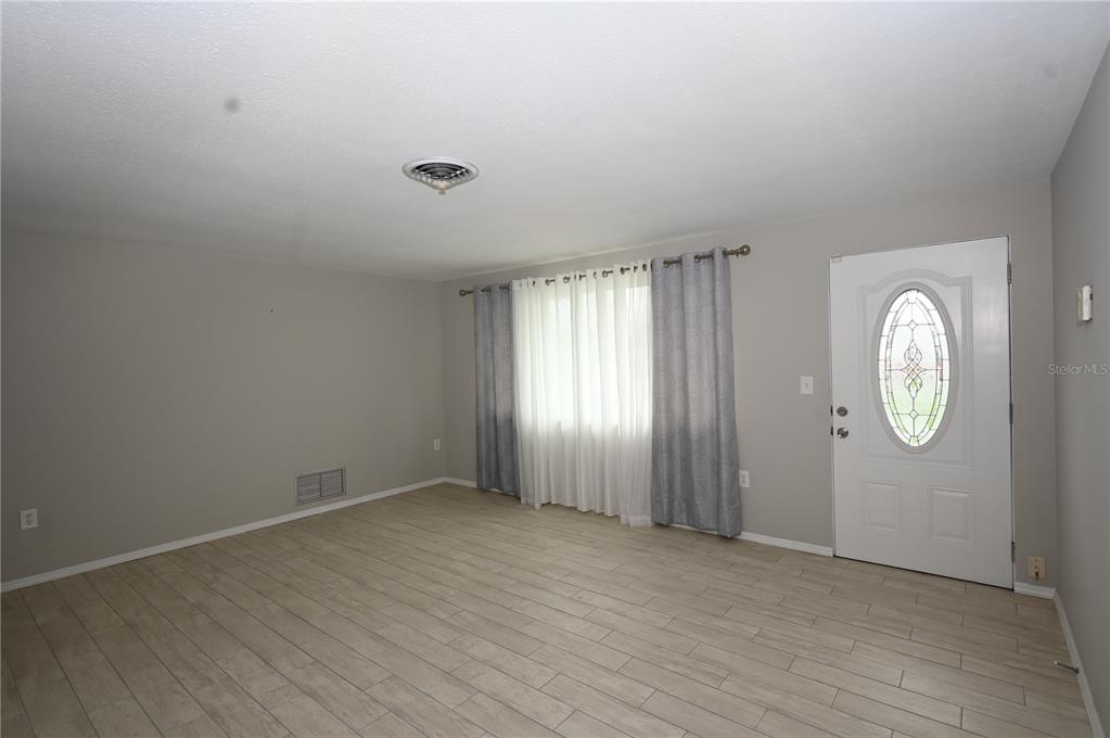 An empty living room features light wood-look tile flooring, gray walls, and a front door — 1620 MORNING DOVE LANE, ENGLEWOOD, FL