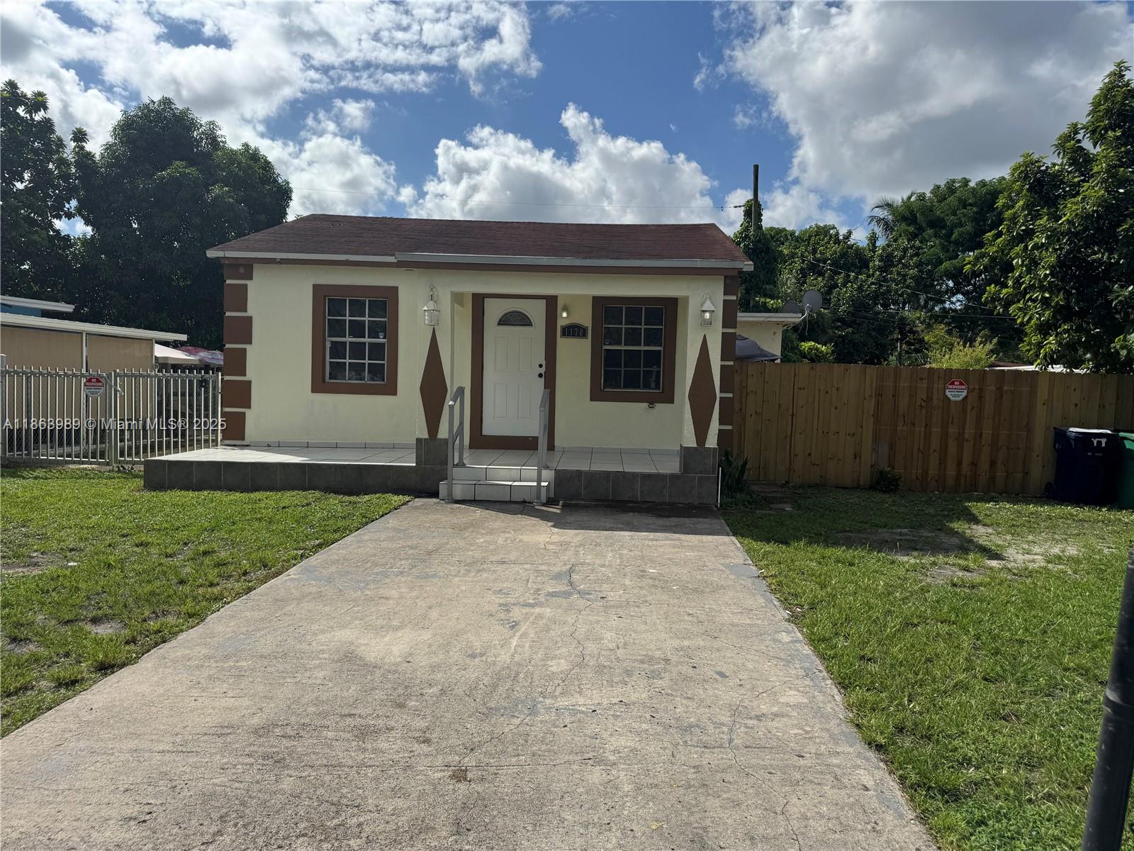 A single-story house with a concrete driveway, tiled porch, and brown trim under a cloudy sky — 1178 NW 105th Ter, Miami FL 33150, MIAMI, FL
