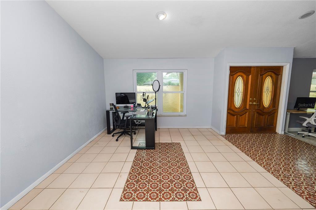 A room with light-colored tile flooring, a desk, a patterned rug, and double wooden doors — 2010 MOSS COURT, DUNEDIN, FL