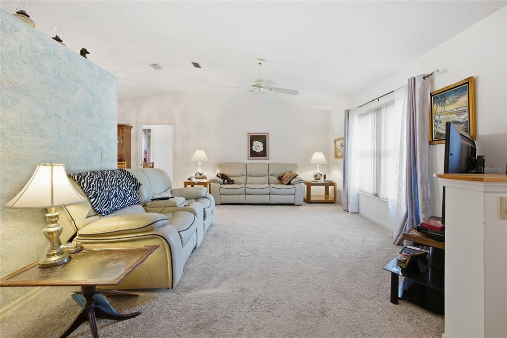 A living room features light-colored leather sofas, beige carpeting, and a ceiling fan — 712 MAGNOLIA AVENUE, INVERNESS, FL