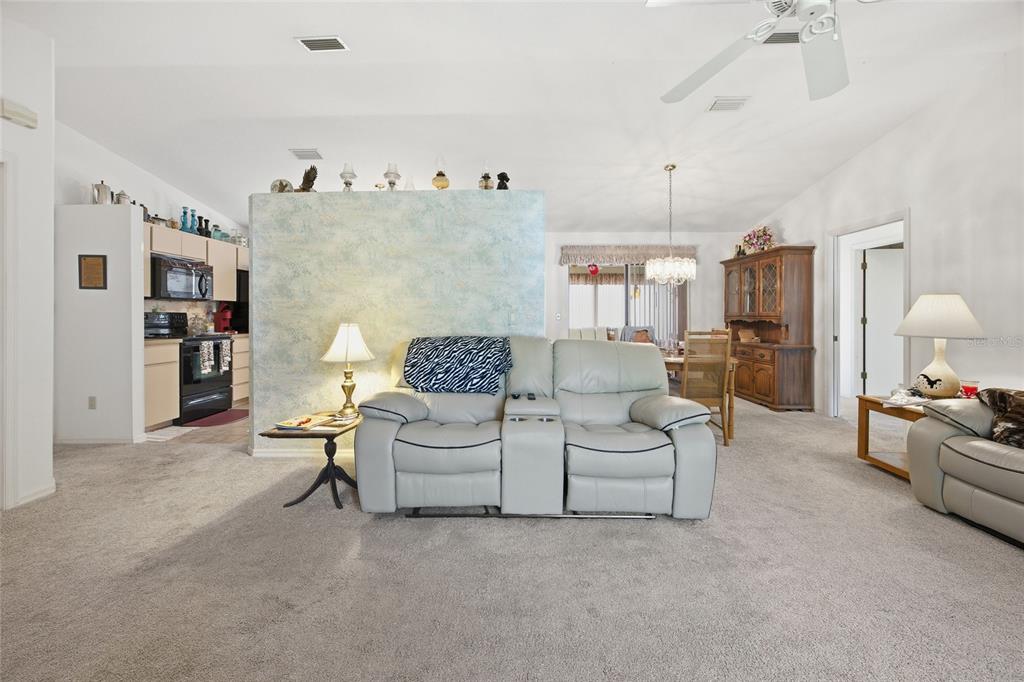 A living room features a light blue partition wall, gray carpet, and a reclining sofa — 712 MAGNOLIA AVENUE, INVERNESS, FL