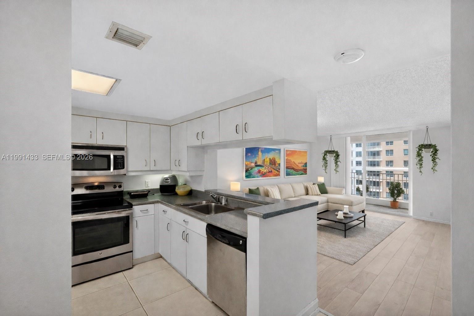 A kitchen with white cabinets and stainless steel appliances opens into a living area — 701 Brickell Key Blvd # 1108, Miami FL 33131, MIAMI, FL