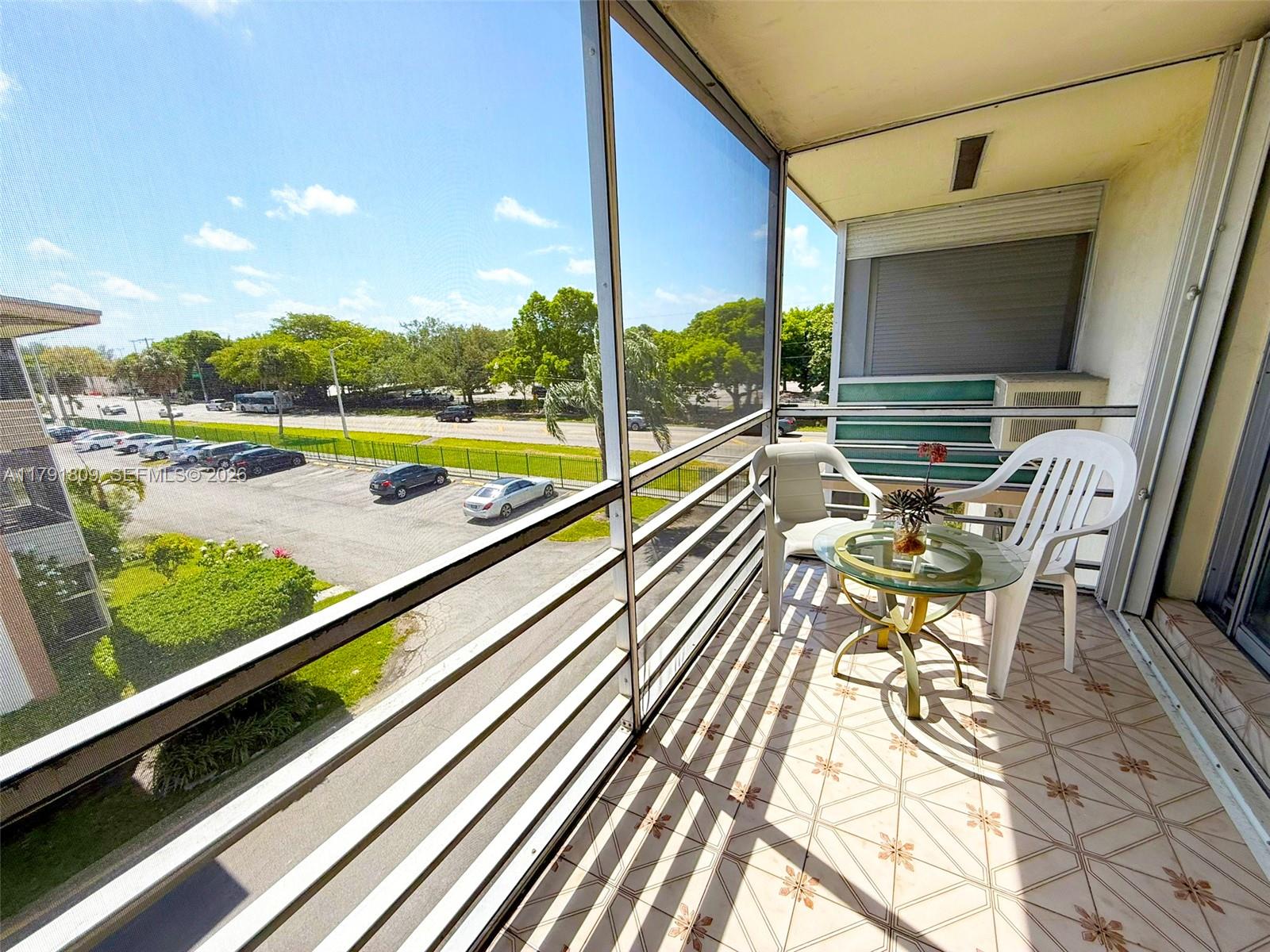 A screened-in balcony features tiled flooring, a small glass table, and two white plastic chairs — 1355 NE 167th St # 302, Miami FL 33162, MIAMI, FL