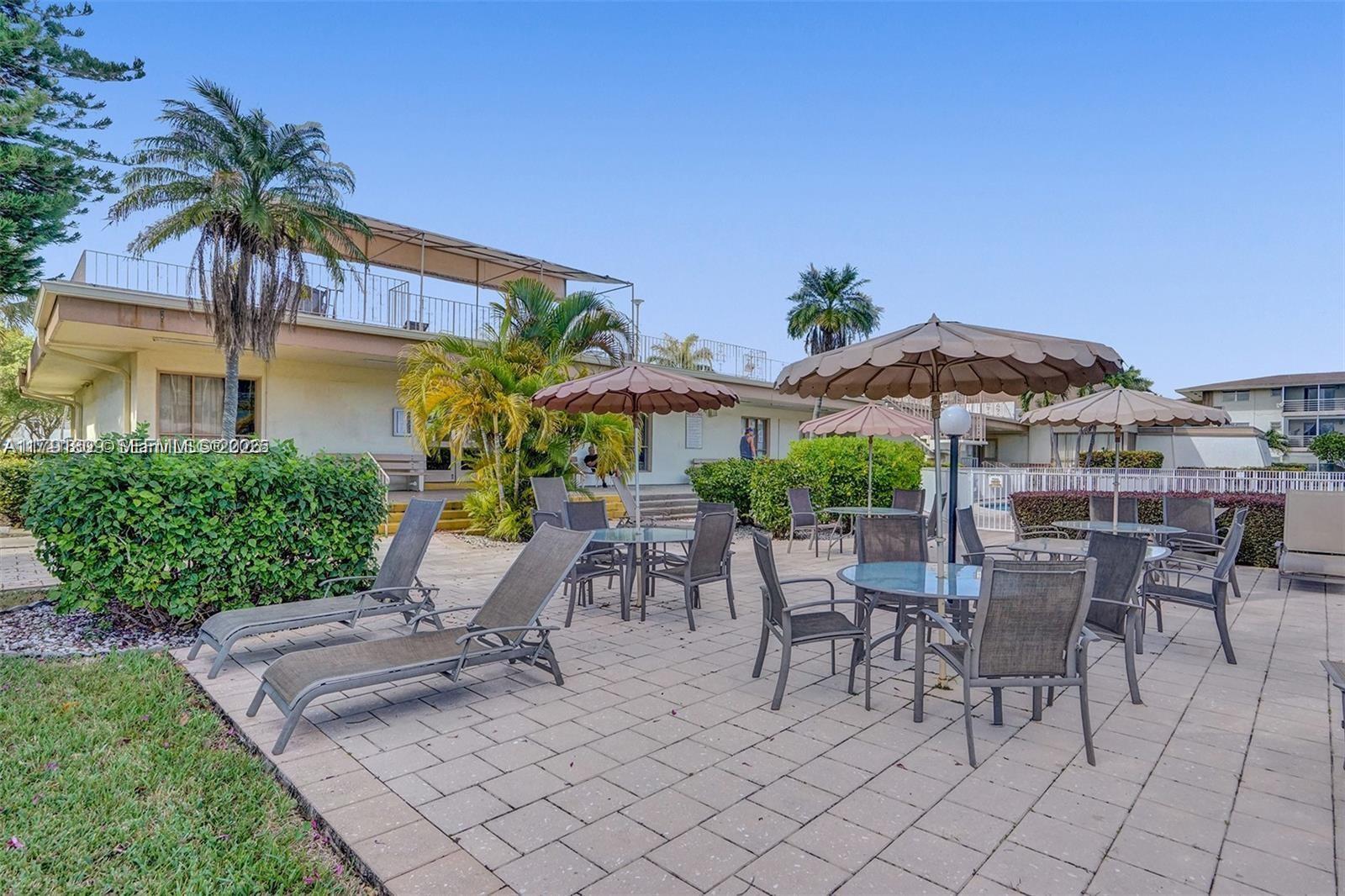 An outdoor patio area features lounge chairs, tables with umbrellas, and a building exterior — 1355 NE 167th St # 302, Miami FL 33162, MIAMI, FL