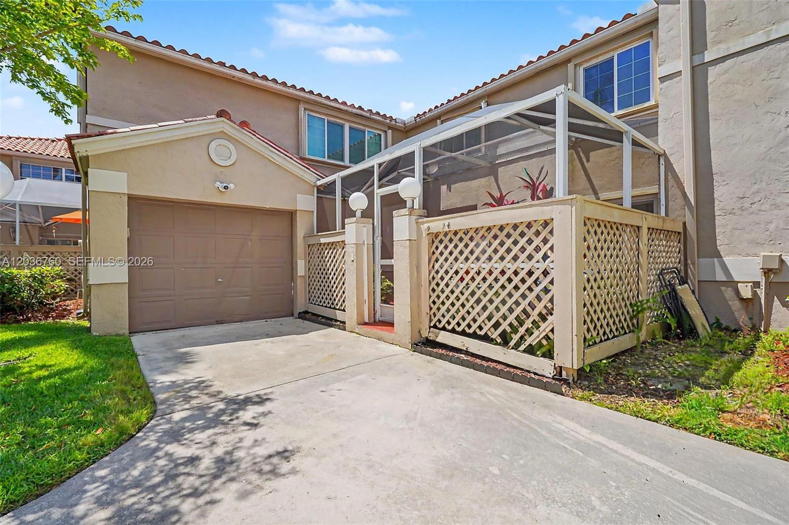 A tan townhouse exterior features a single-car garage and a screened-in front patio area — 10994 Neptune Dr, Cooper City FL 33026, COOPER CITY, FL