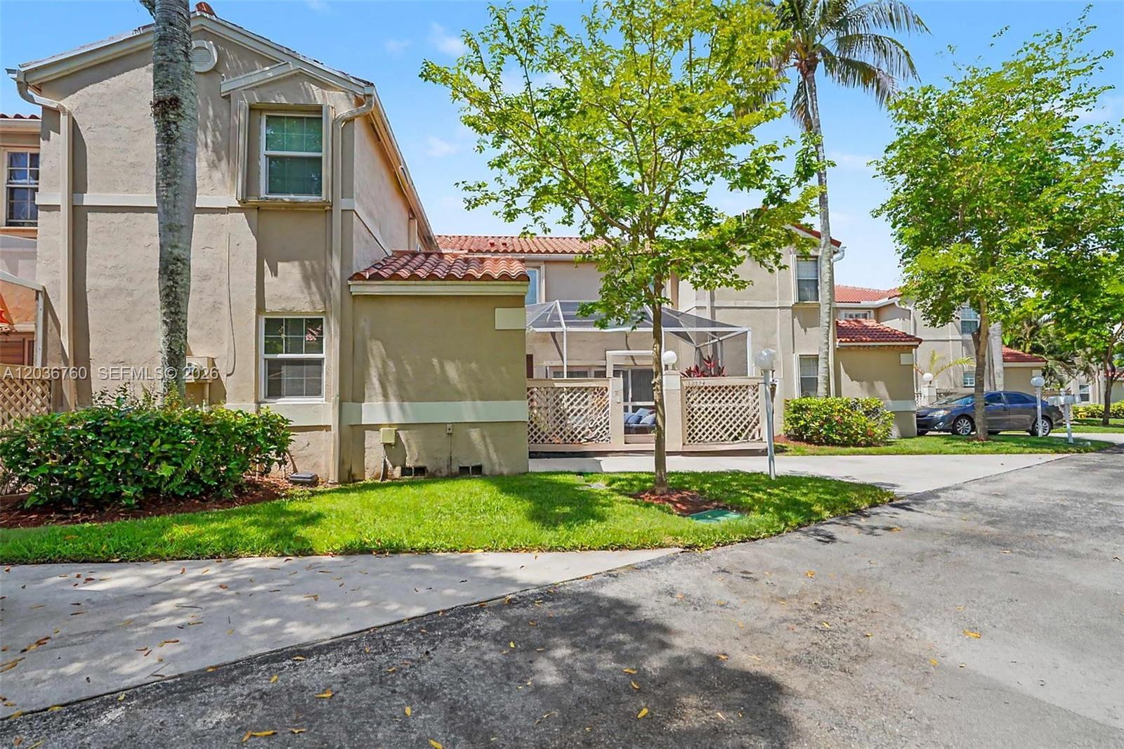 A two-story tan stucco townhouse features a screened-in patio and a small front lawn — 10994 Neptune Dr, Cooper City FL 33026, COOPER CITY, FL