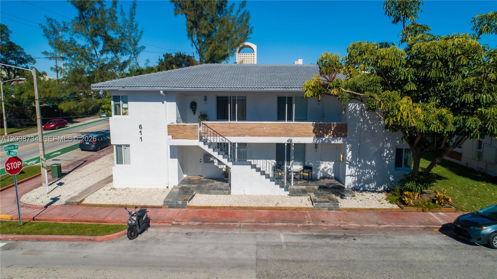 A two-story white apartment building features an exterior staircase and a stone-tiled ground level — 611 74th St, Miami Beach FL 33141, MIAMI BEACH, FL